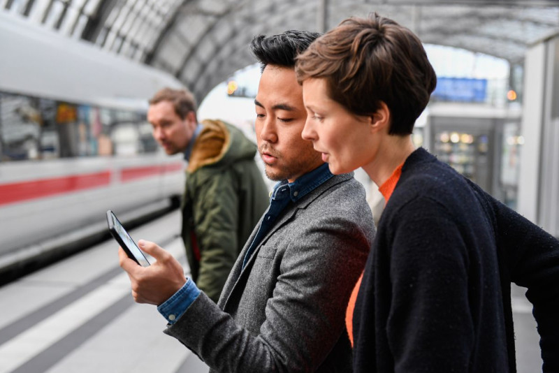 Zwei Menschen schauen gemeinsam an einem Bahnhof auf ein Handy
